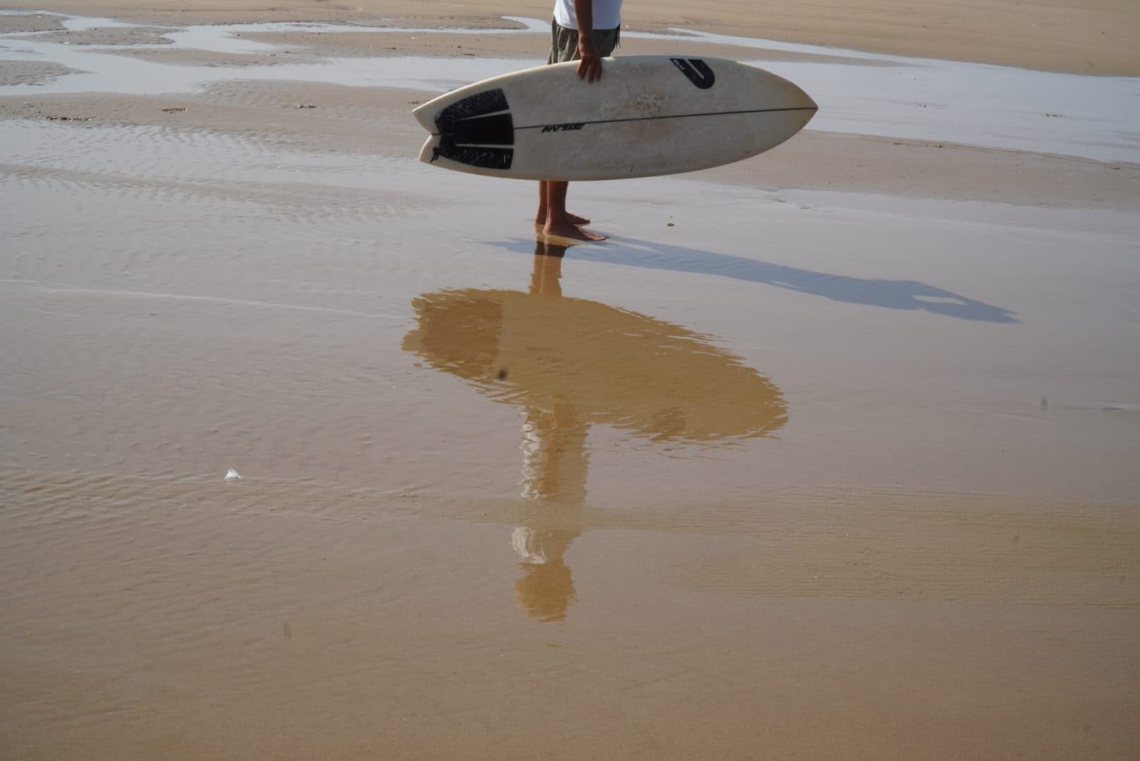 A surfboard standing in the wet sand, reflected at low tide