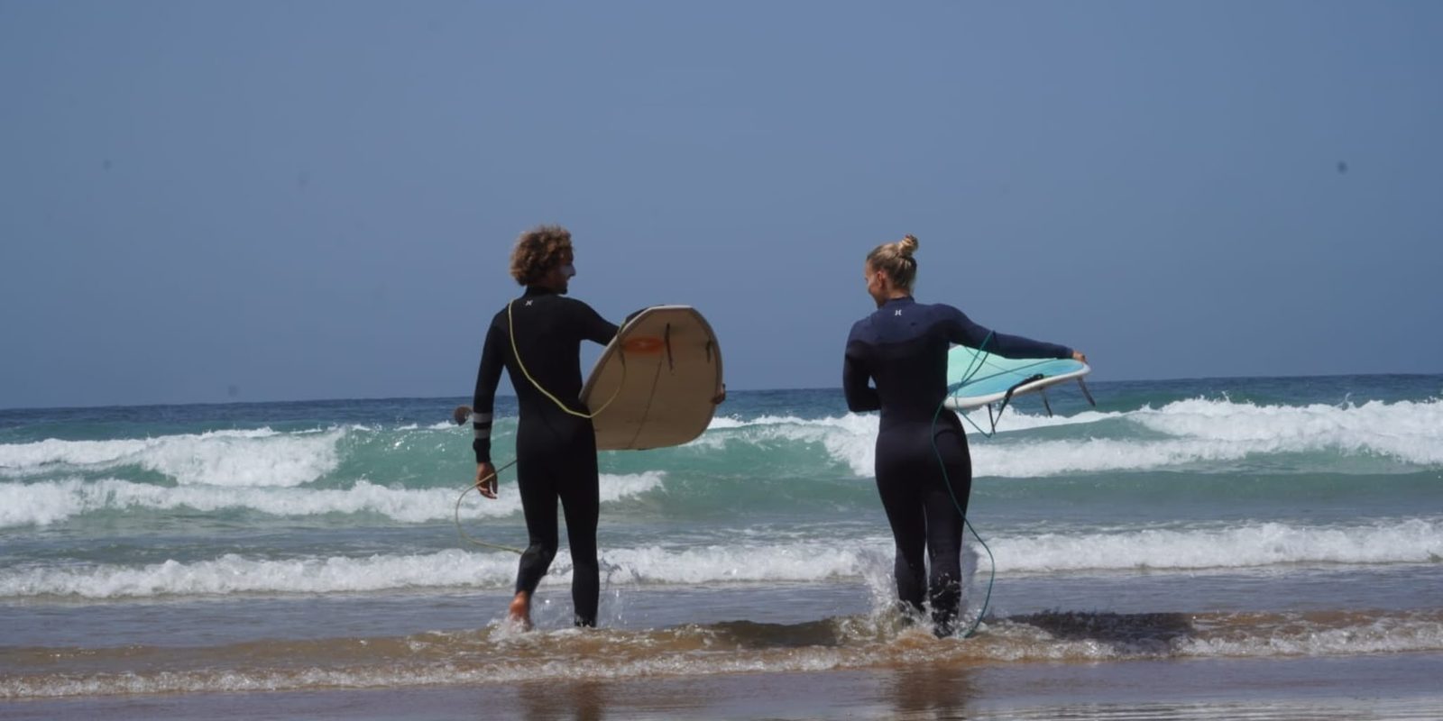 Two surfers walking into the Atlantic with their boards