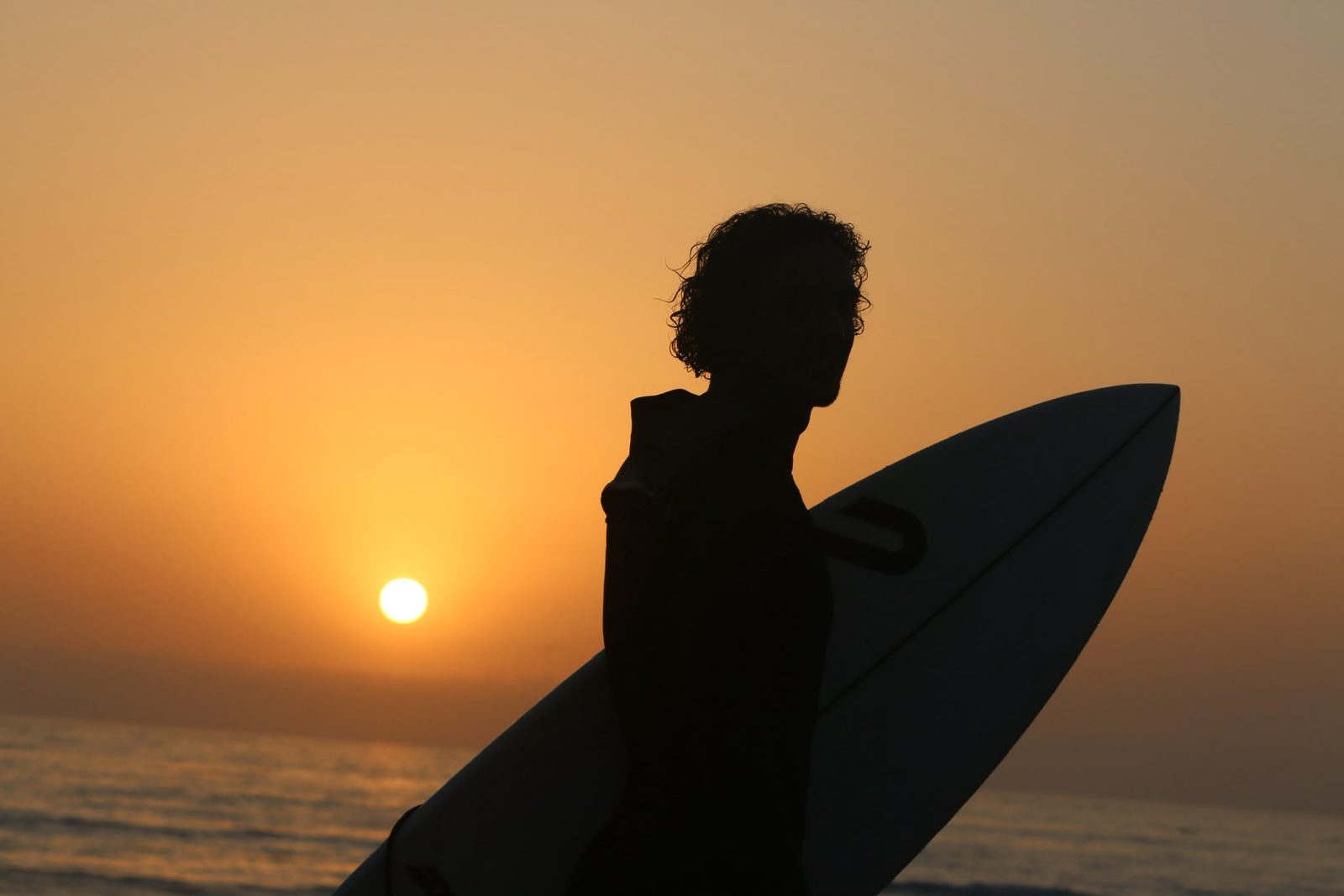 A surfer silhouetted against the sunset with a board