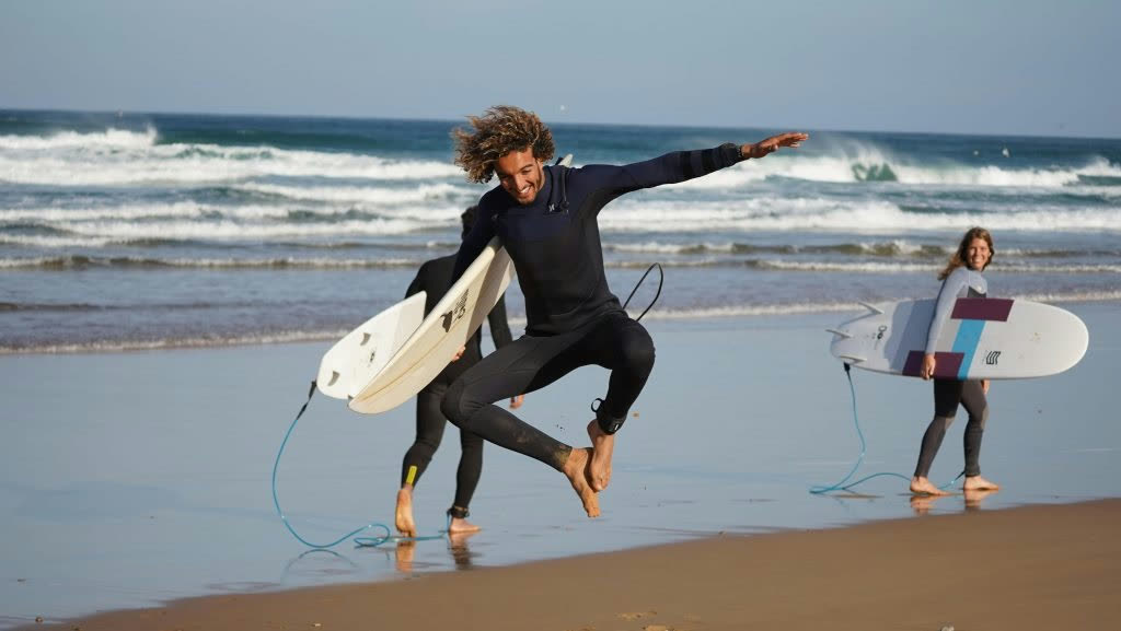 Surf coach Youness running into the Atlantic with a student at Taghazout
